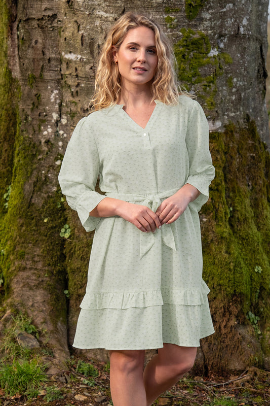 Lifestyle image of female model stood in front of a tree wearing a green ruffle dress