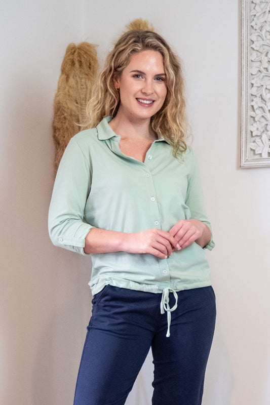 Lifestyle image of female model wearing a green button top and blue trousers