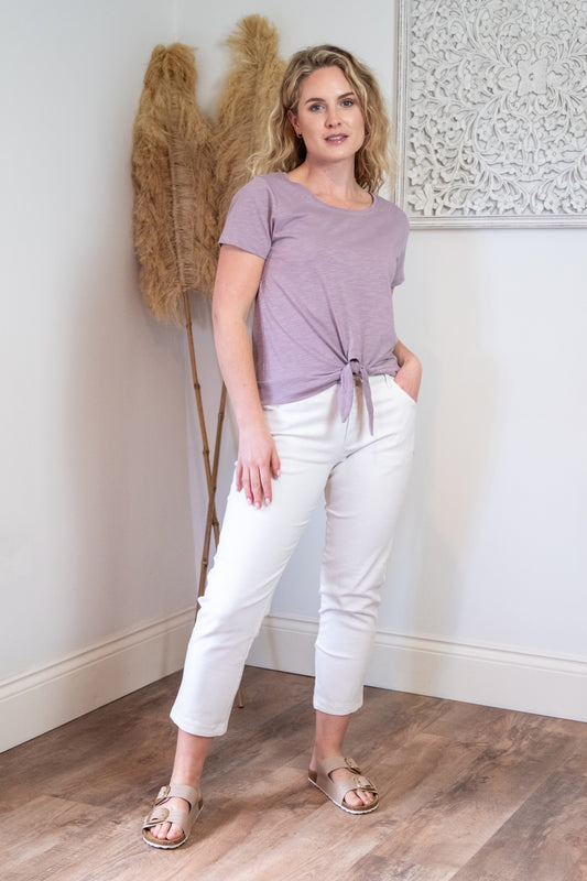 Lifestyle image of female model wearing white chino trousers and mauve tie waist top