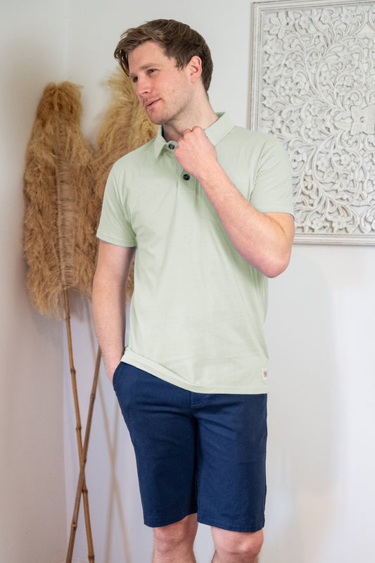 Lifestyle image of male model wearing a Rupert and Buckley Theo green polo top and navy blue chino shorts