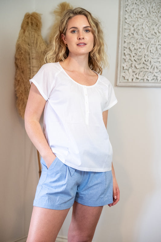Lifestyle image of a female model wearing a white Rupert and Buckley woven top and blue chambray shorts