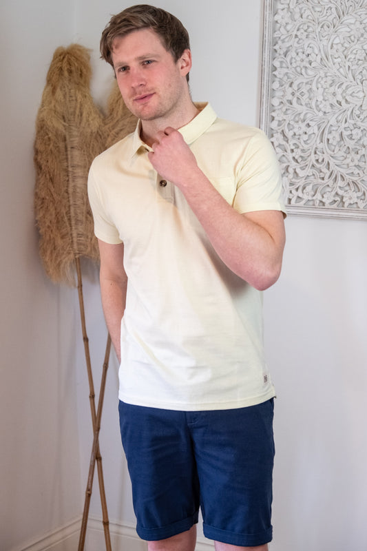 Lifestyle image of male model wearing Rupert and Buckley Theo jersey polo shirt in Ecru and navy chino shorts